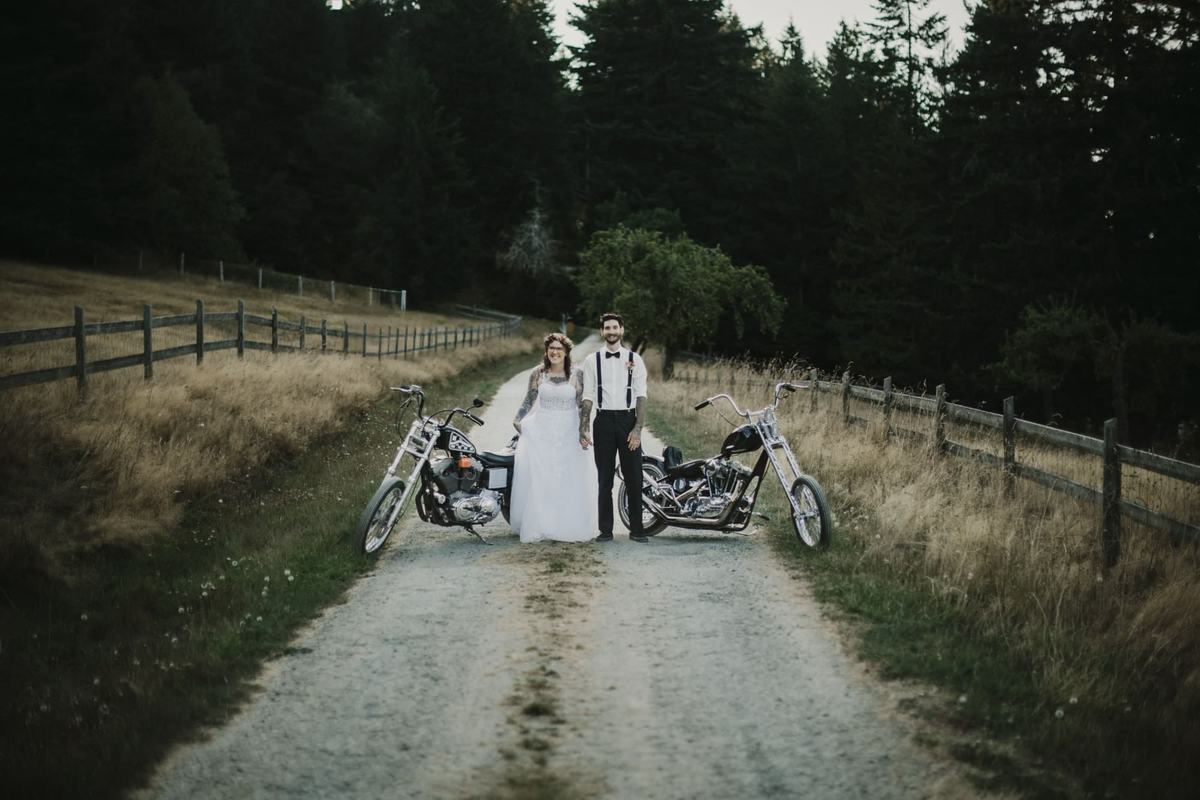 Newlyweds flanked by two motorcycles on a gravel road