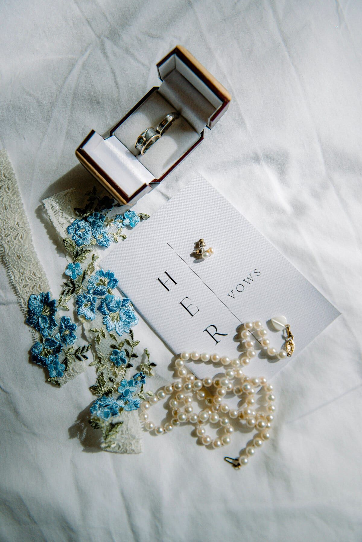 Flat lay of rings, pearls, blue garter and her vow book