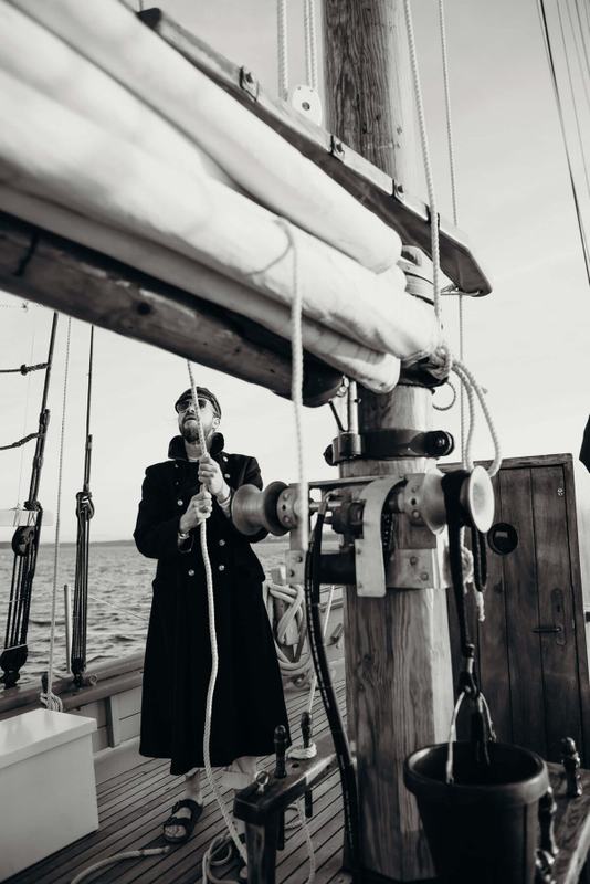 Crew member in a long coat hauling a line at the mast