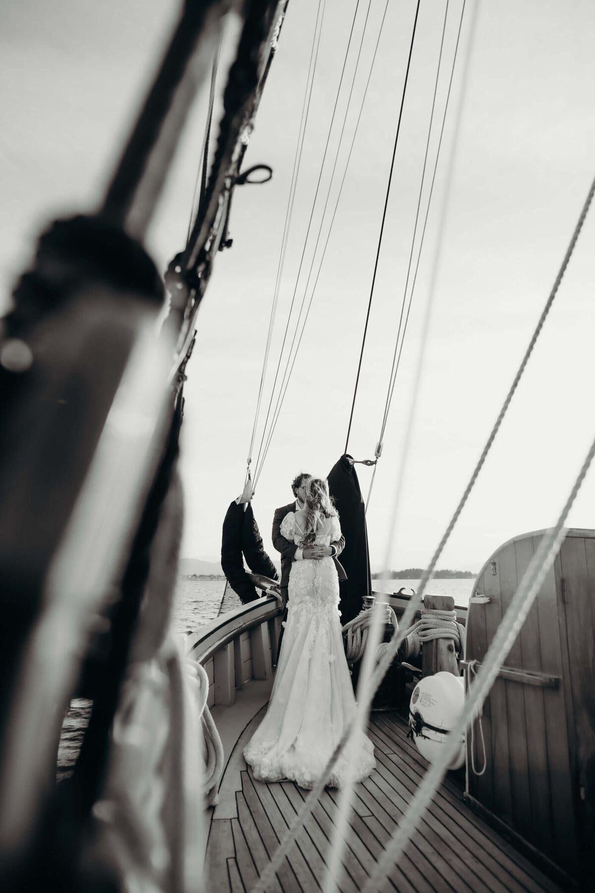 Couple embracing at the bow, framed down the rope-lined deck
