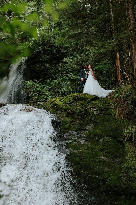 Newlyweds on a mossy ledge beside a rushing rainforest waterfall