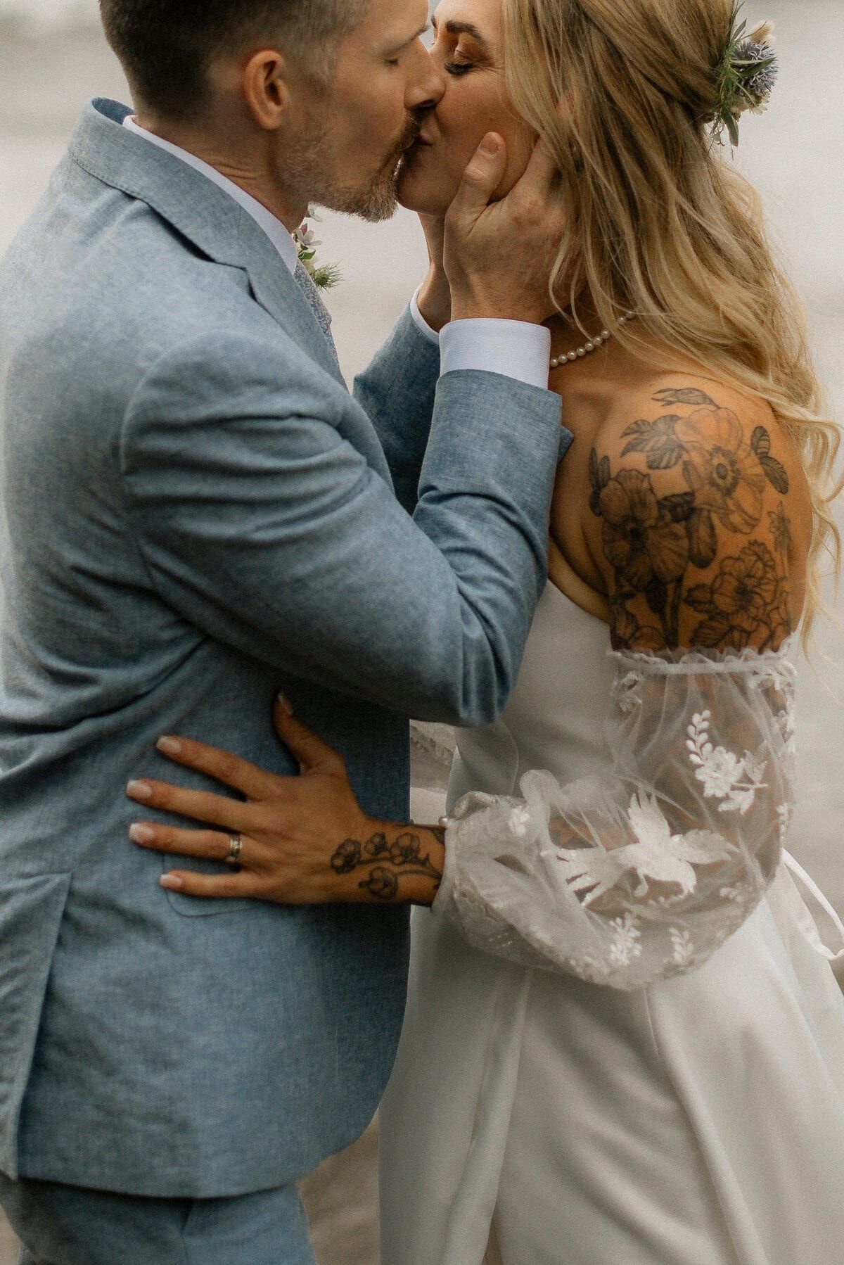 Close-up of a couple kissing, lace sleeves and tattooed shoulder showing