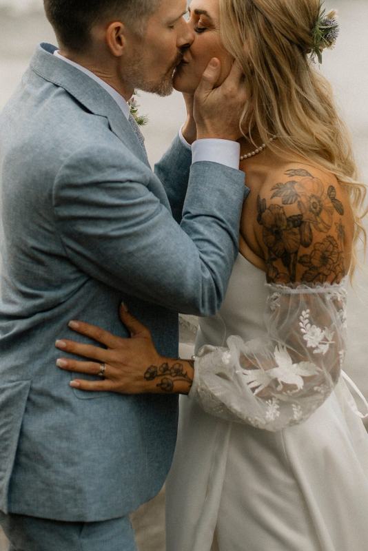 Close-up of a couple kissing, lace sleeves and tattooed shoulder showing