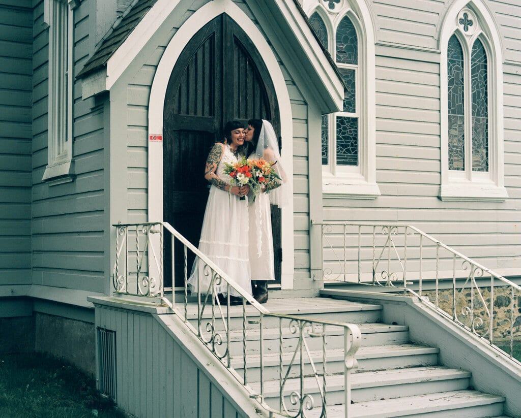 Newlyweds kissing in the arched doorway of a pale green church