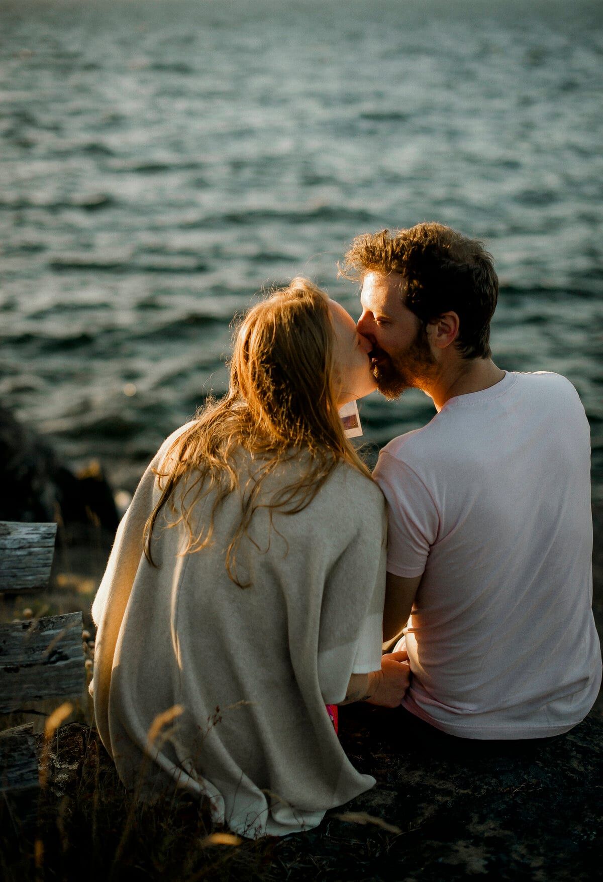 Couple kissing on shoreline rocks at sunset by the water