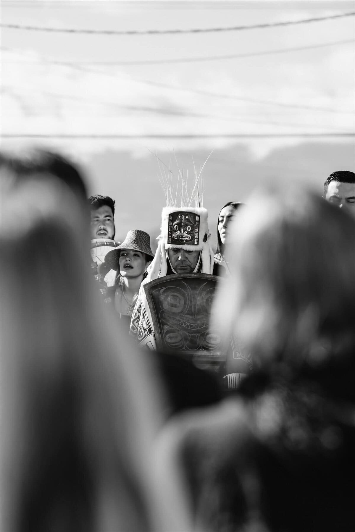 Black-and-white glimpse of a regalia dancer between watching guests