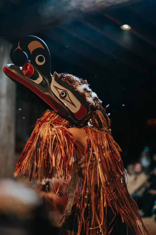 Dancer in a carved raven mask with flowing cedar-toned fringe