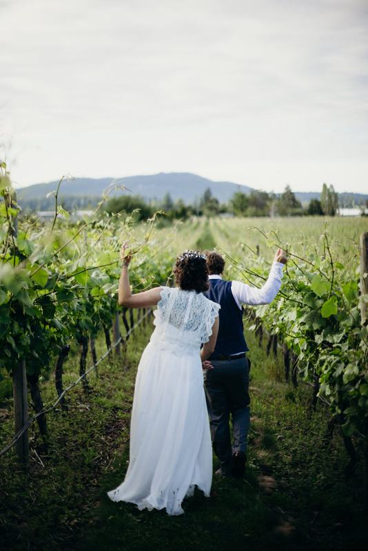 Couple raising arms triumphantly between vineyard rows, mountains beyond