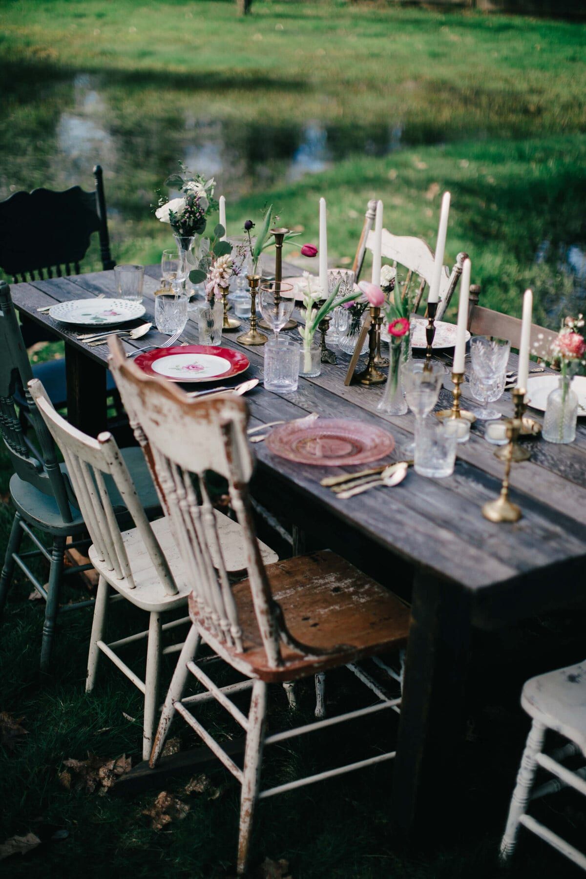 Mismatched farmhouse chairs around a candlelit pond-side table
