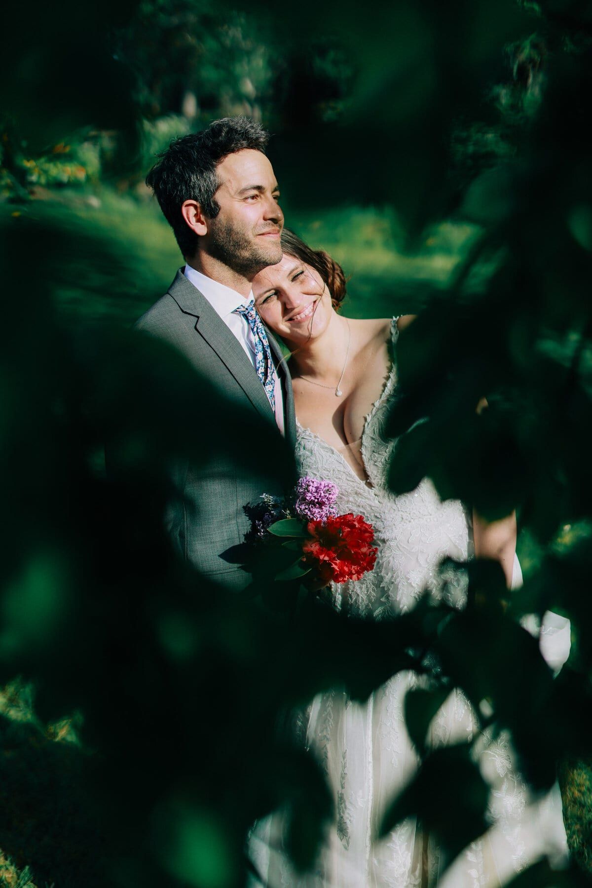 Sunlit portrait framed by leaves, bride nestled against the groom