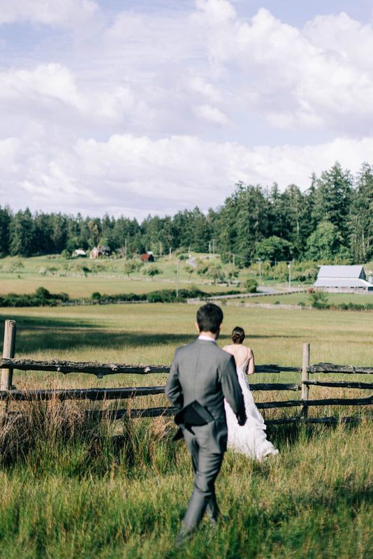Groom following his bride through tall grass along the fence