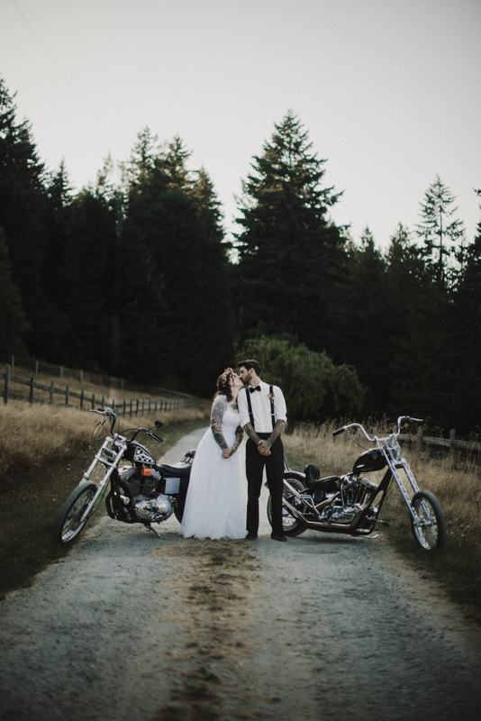Newlyweds kissing between two motorcycles on a gravel country road