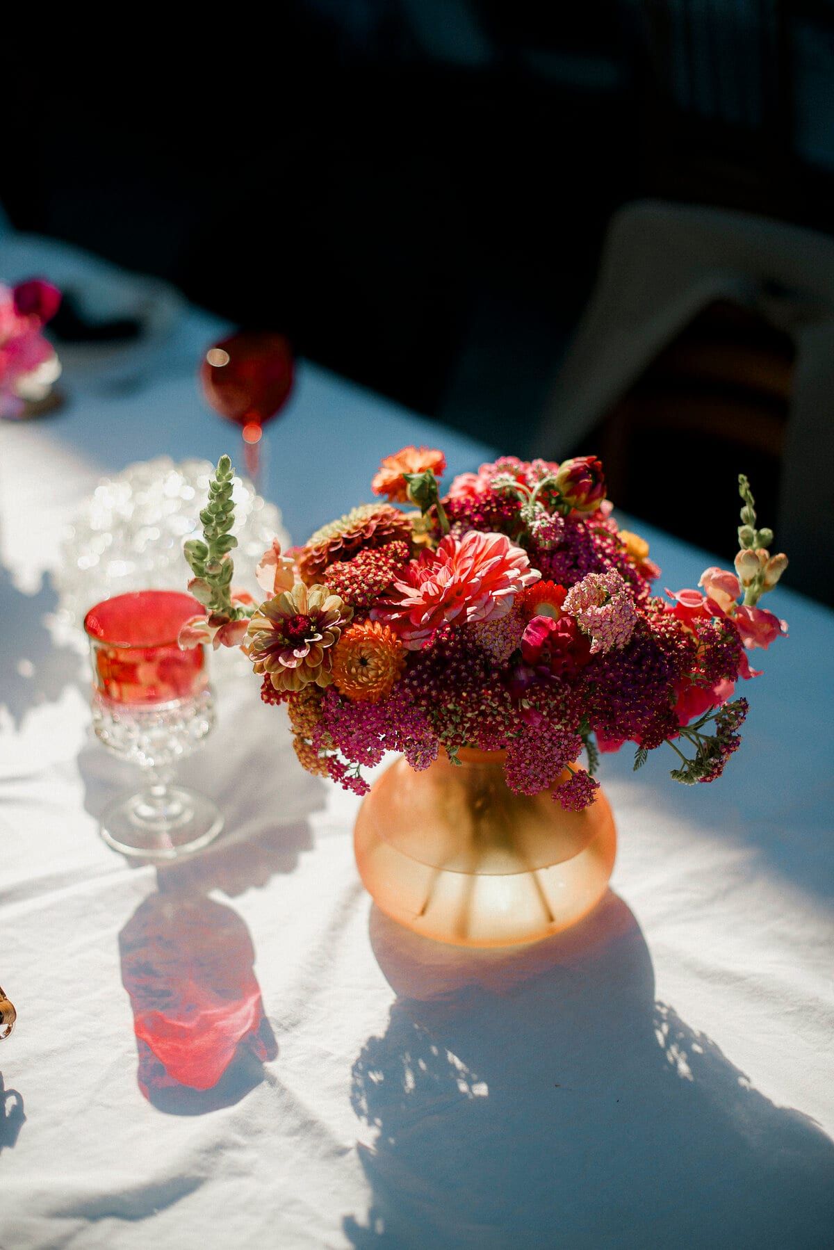 Sunlit centrepiece of red and pink dahlias on white linen