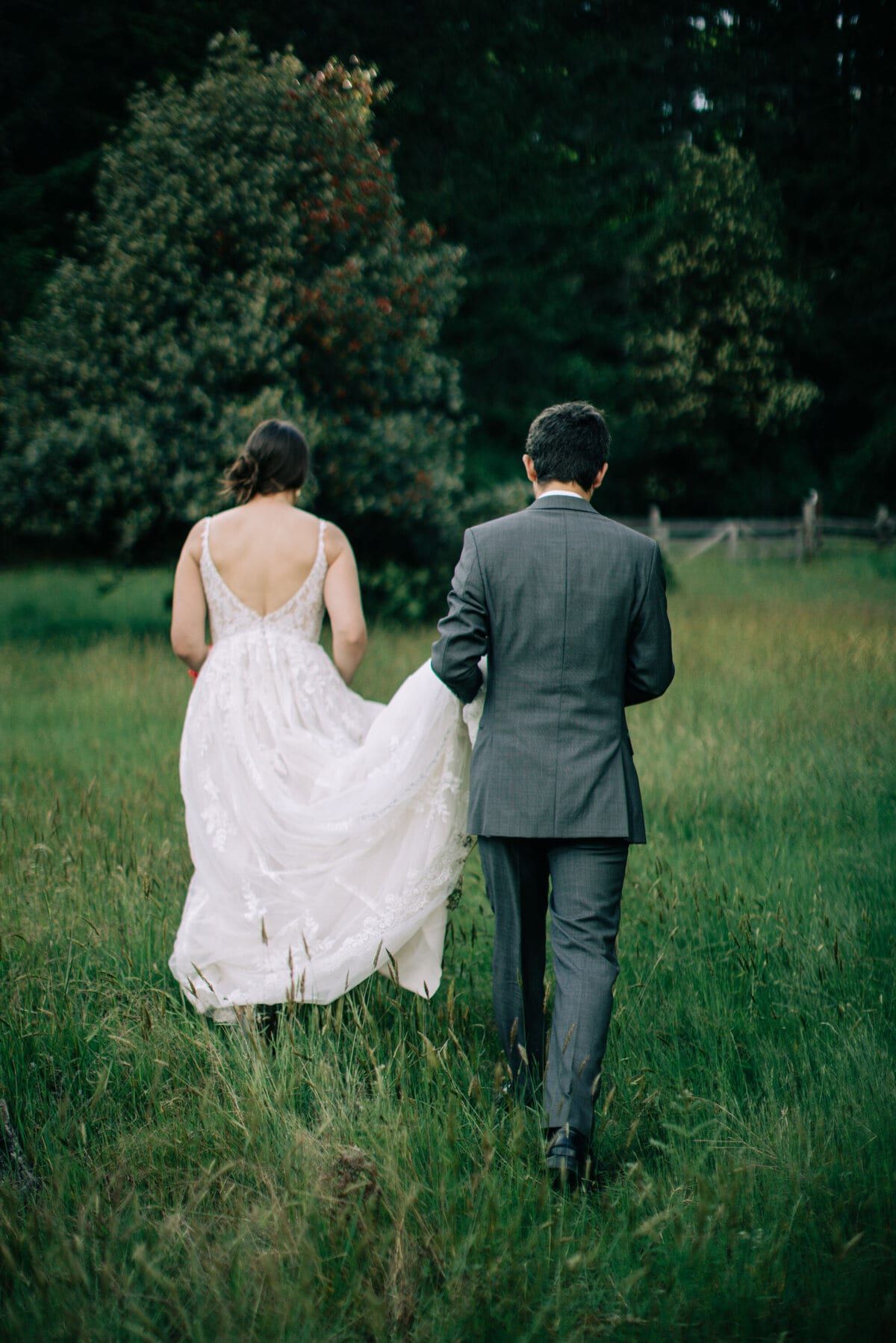 Groom carrying the lace train as they cross the field