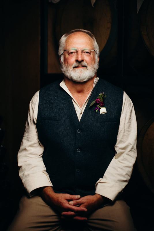 Silver-bearded man in a wool vest wearing a boutonniere