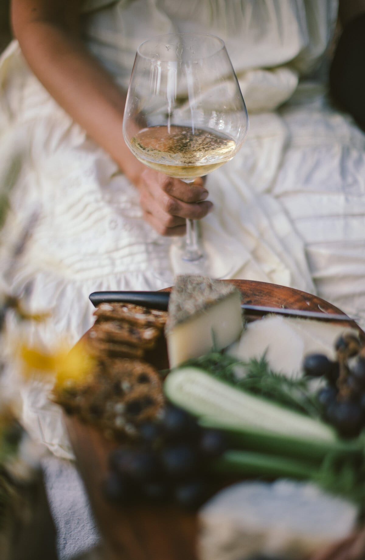 Glass of cider raised above a rustic cheese board