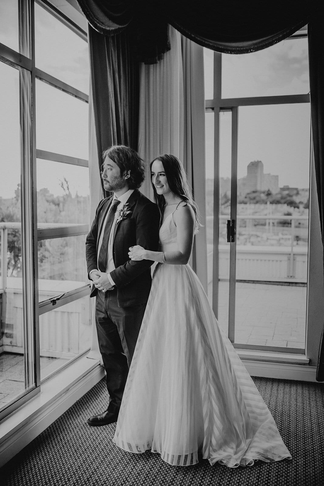 Couple arm in arm gazing out a tall hotel window