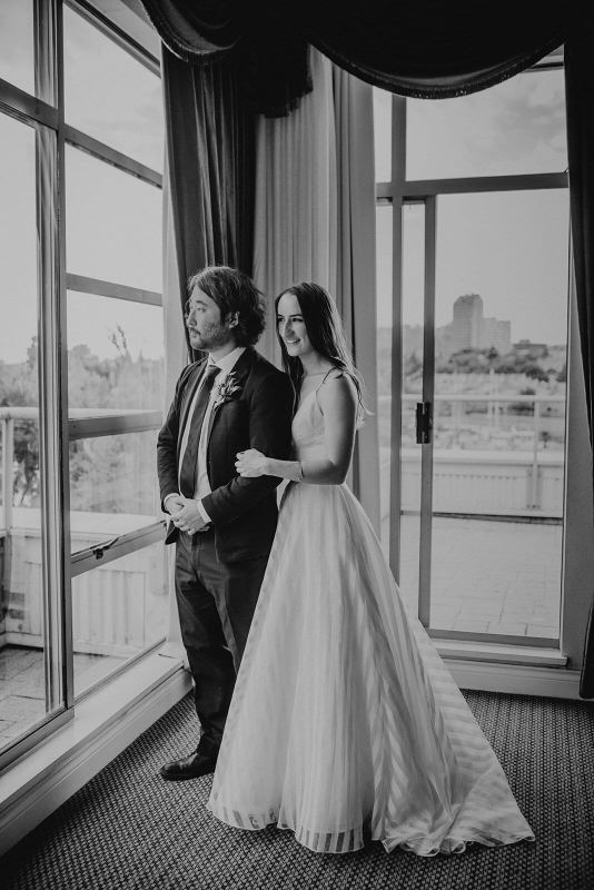 Couple arm in arm gazing out a tall hotel window