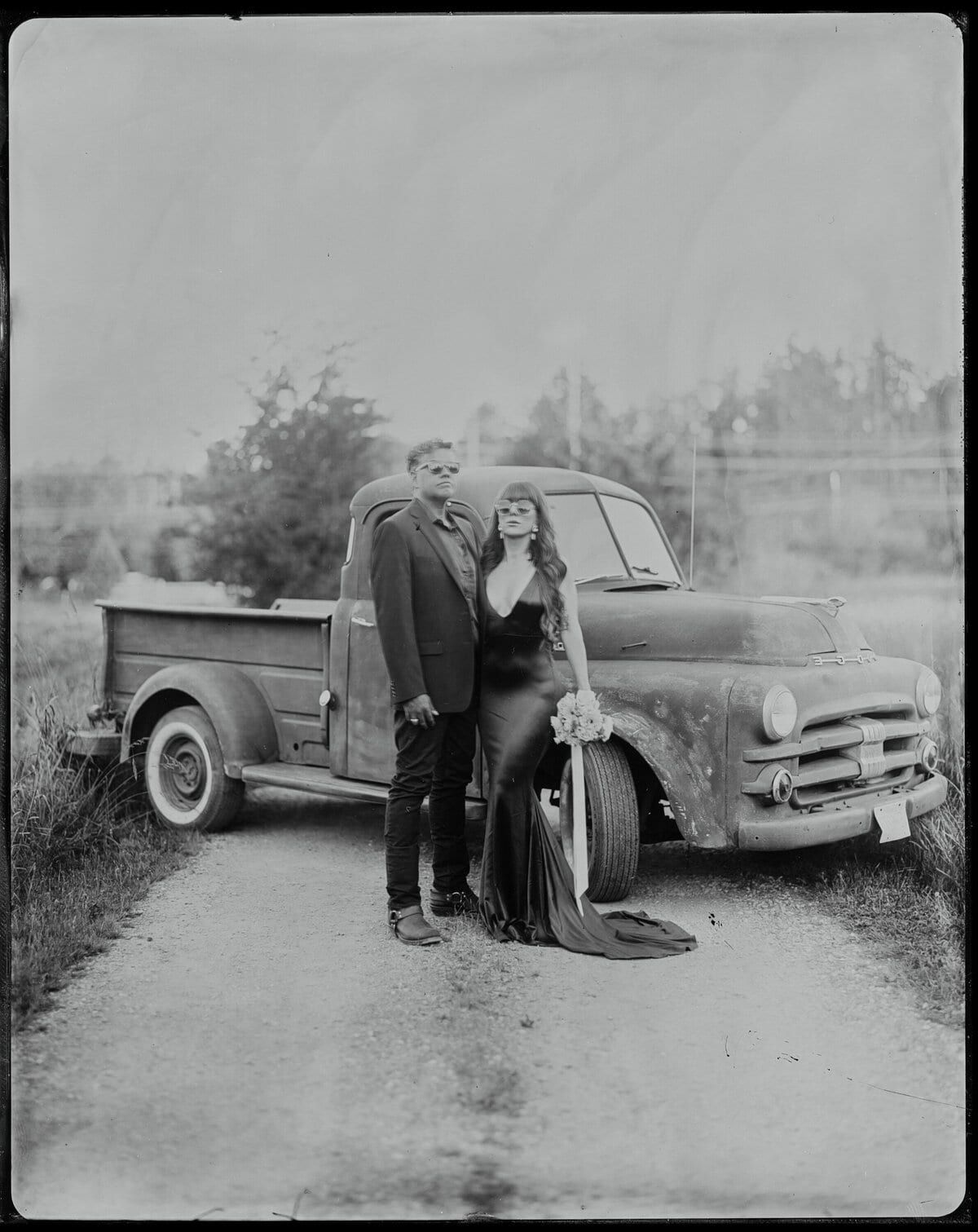 Pair posed beside a vintage pickup truck on a gravel lane