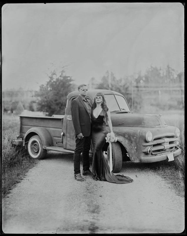 Pair posed beside a vintage pickup truck on a gravel lane
