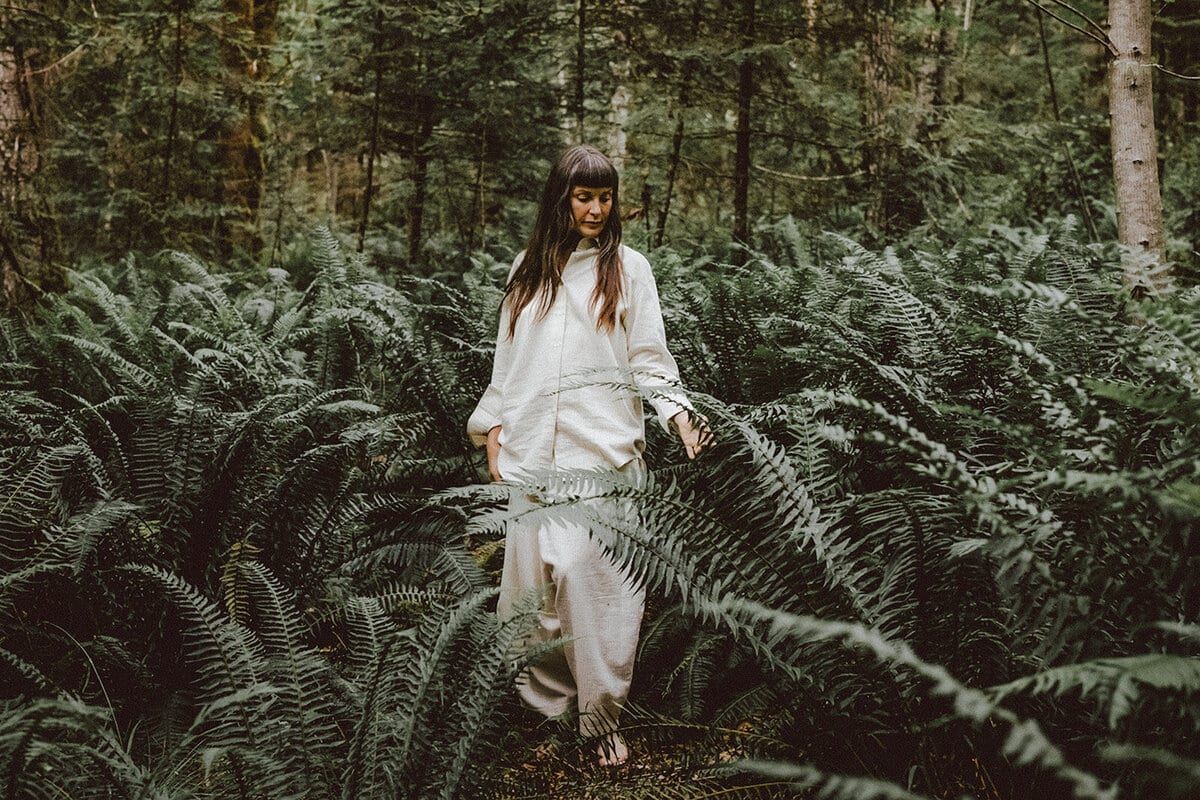 Woman in white walking through chest-high ferns, by Stasia Garraway