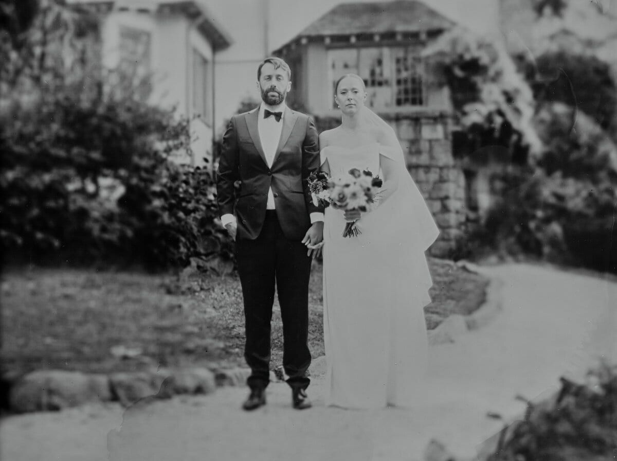 Black-and-white film portrait of newlyweds outside a stone garden house