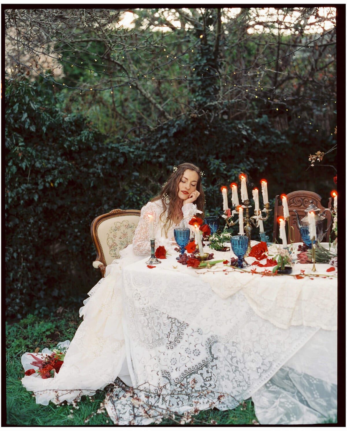 Bride seated at a lace-draped garden table lit by candelabras