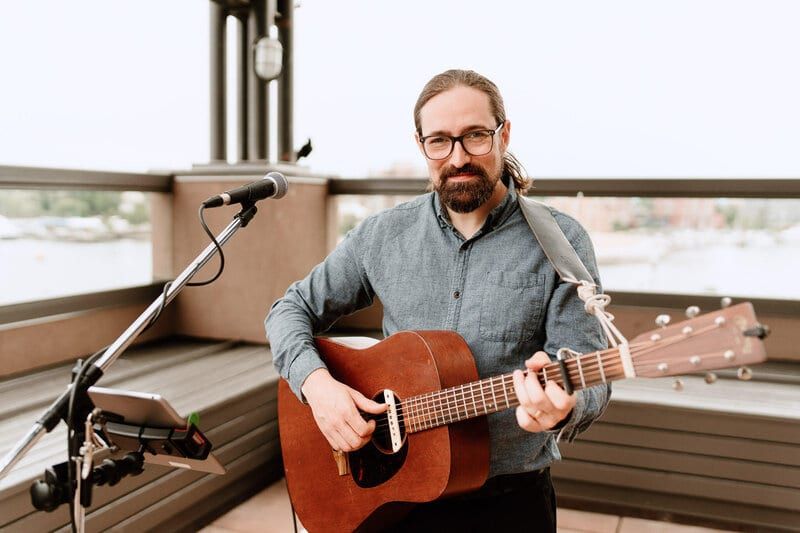 Musician Noah Edwards playing acoustic guitar at a waterfront reception