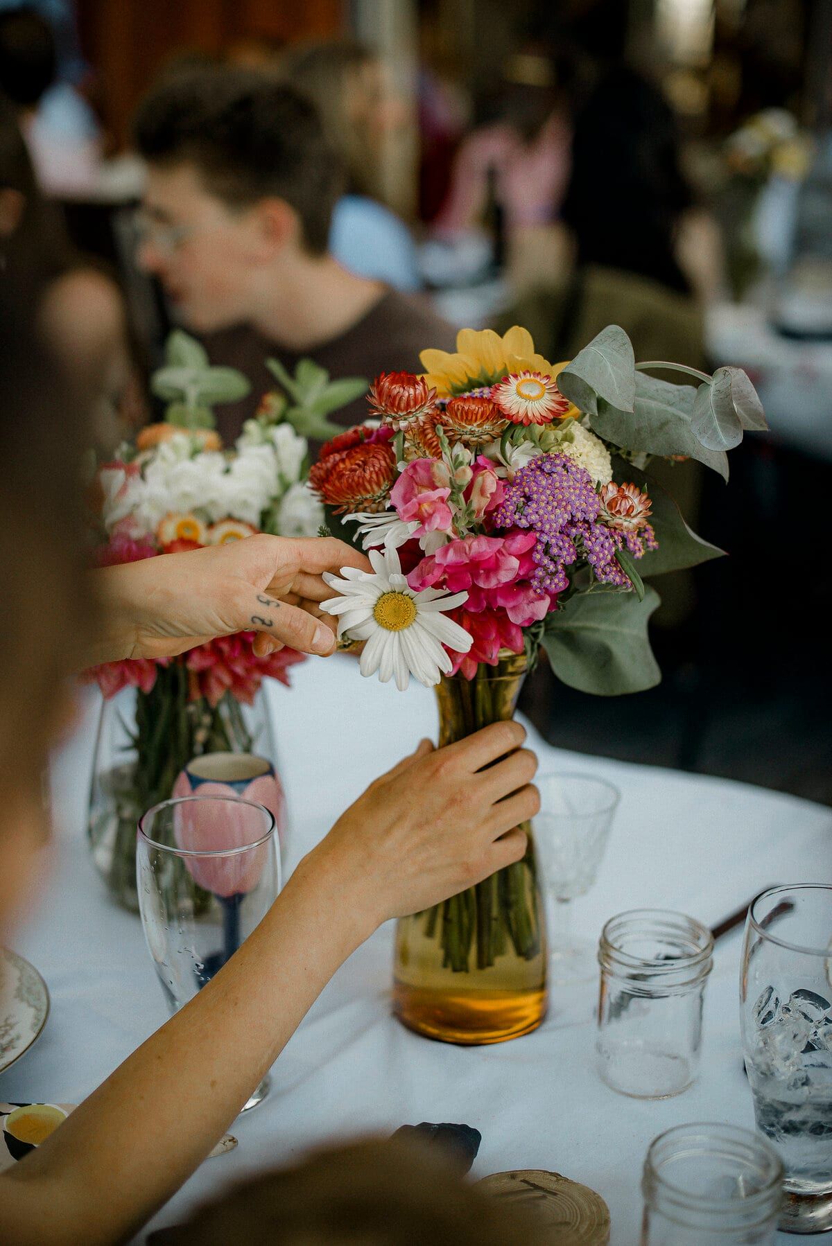 Hands arranging a wildflower centrepiece in an amber vase