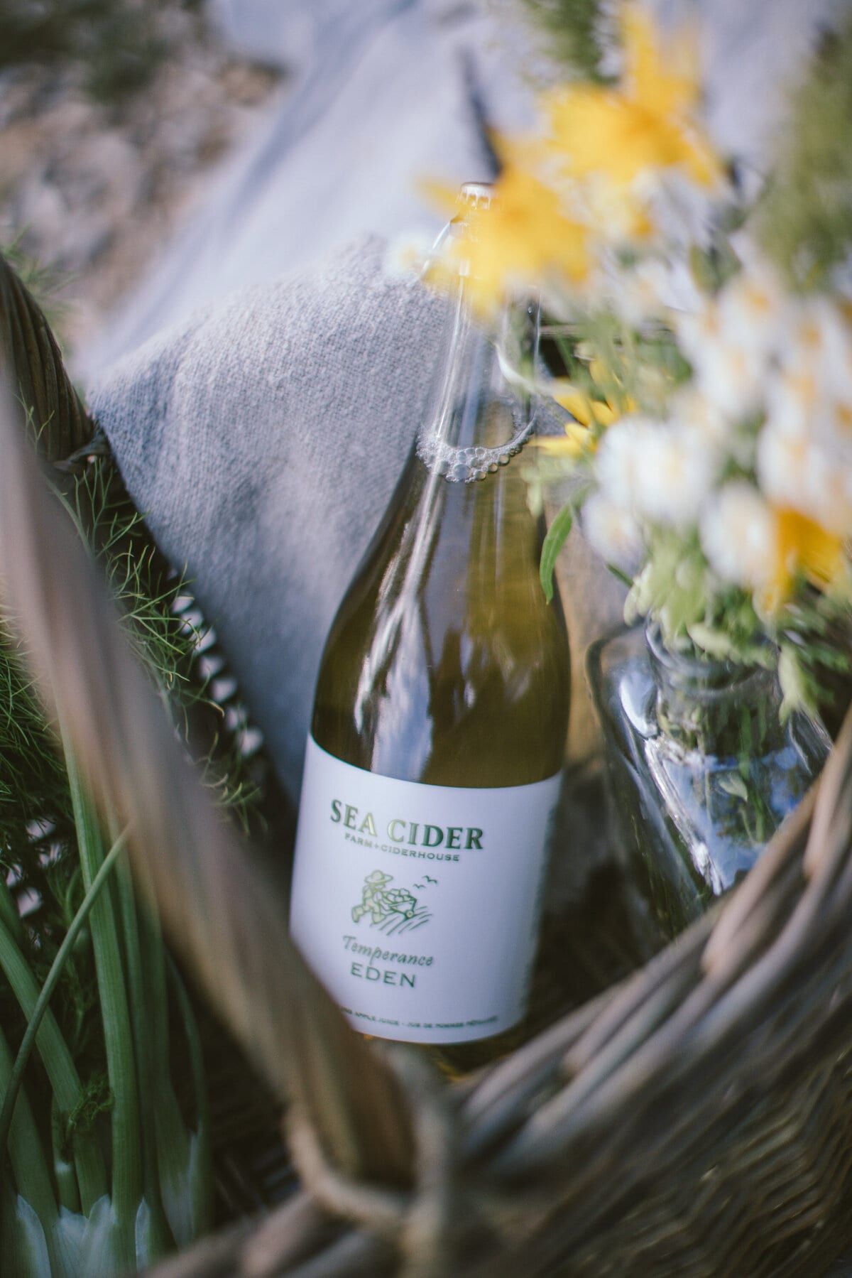 Sea Cider bottle nestled in a picnic basket with wildflowers