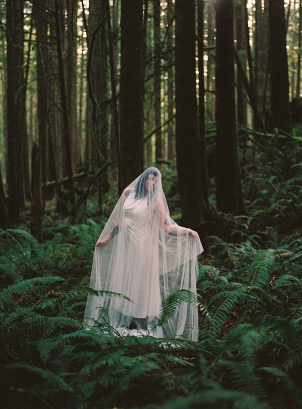 Bride spreading her long sheer veil among forest ferns
