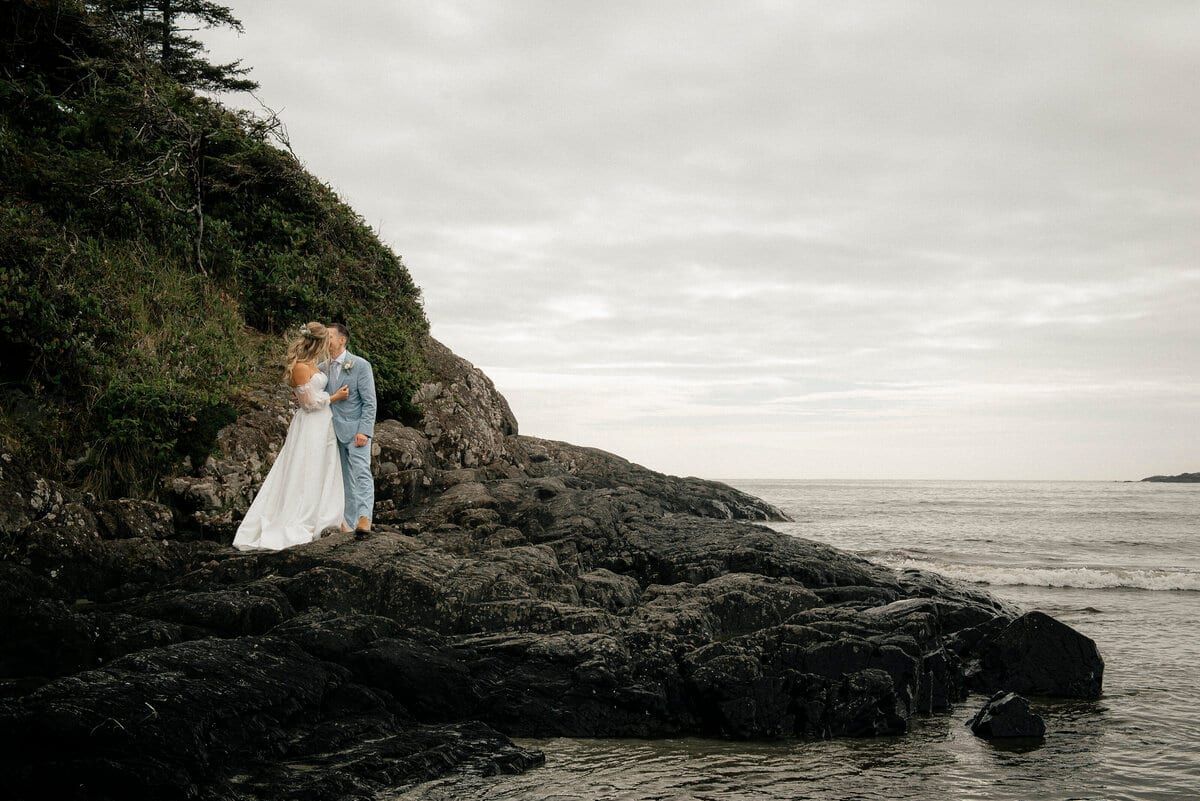 Newlyweds kissing on a rocky headland above the sea