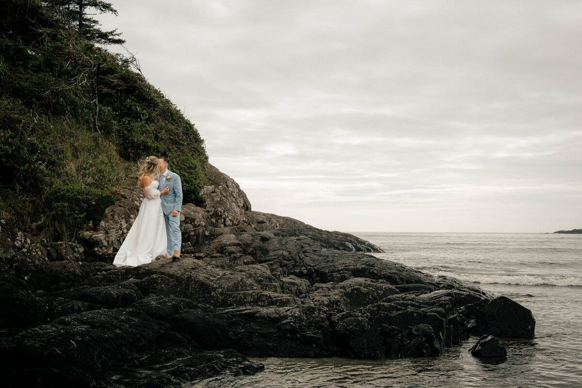 Bride and groom kissing on a rocky headland above the Pacific