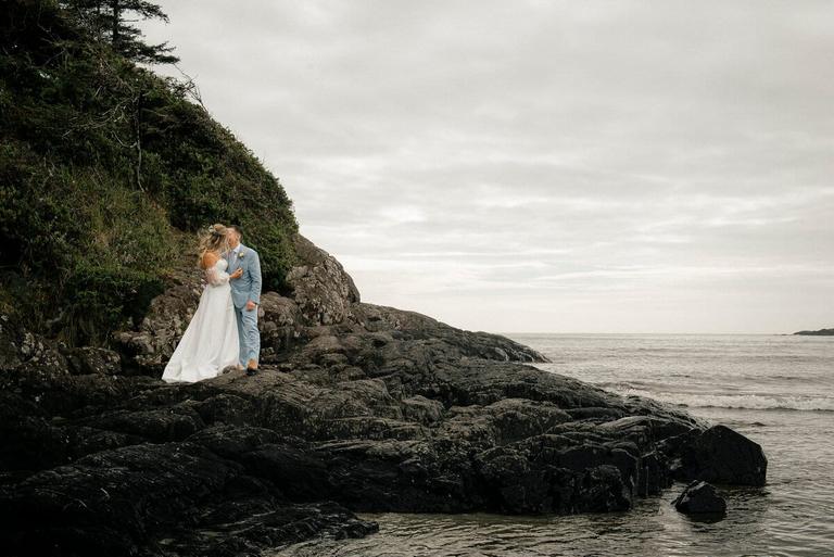 Newlyweds kissing on a rocky headland above the sea