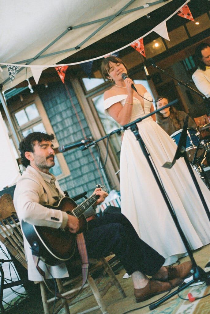 Bride singing at the microphone while a guitarist plays under the tent
