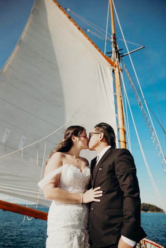 Couple kissing beneath the raised white mainsail