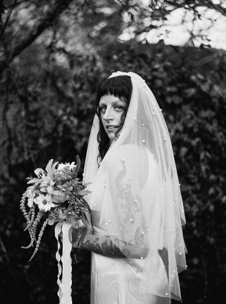 Bride glancing back beneath a pearl-dotted veil, bouquet in hand
