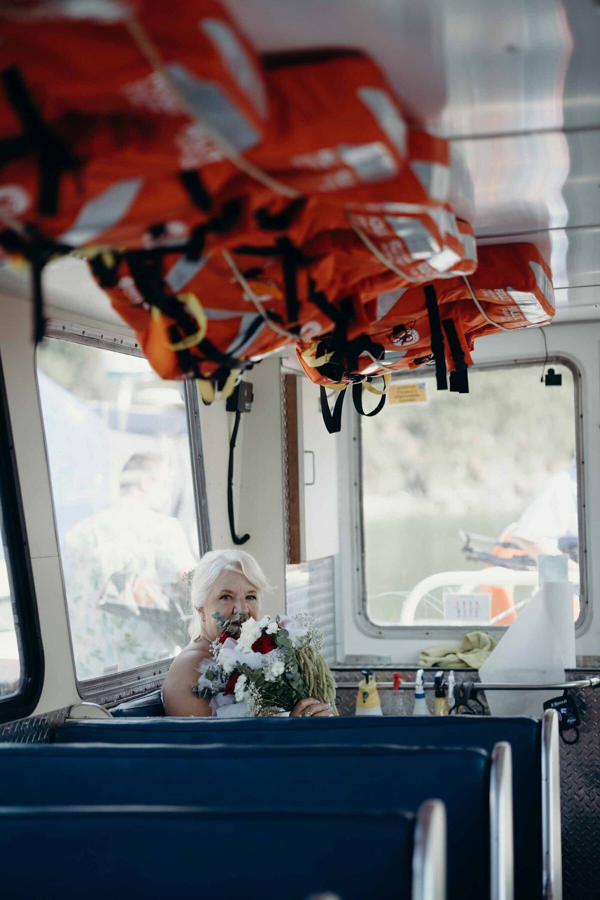 White-haired bride holding her bouquet inside a ferry cabin
