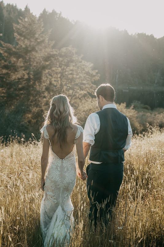 Bride and groom walking hand in hand through golden grass