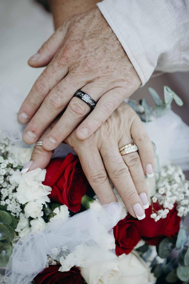 Couple's ringed hands resting together on a red rose bouquet