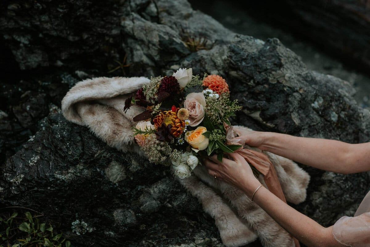 Hands settling an autumn bouquet on a fur wrap over rocks