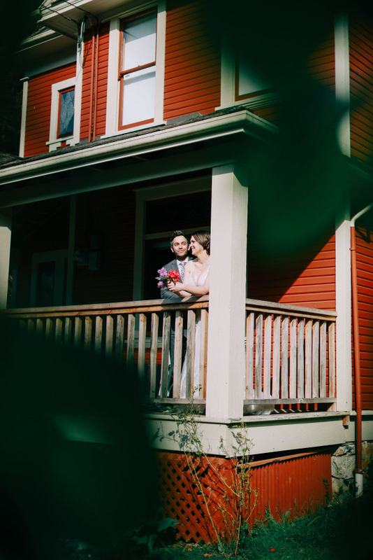 Newlyweds on the covered porch of the red farmhouse