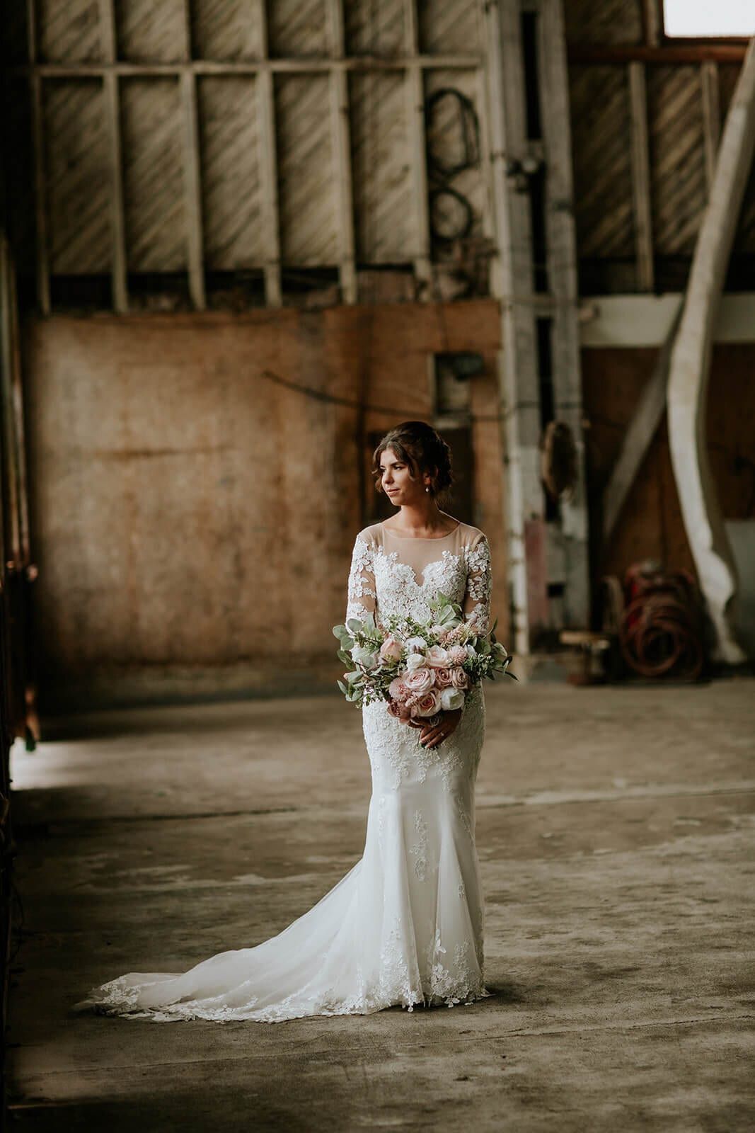 Lace gown trailing across the concrete floor of a rustic barn