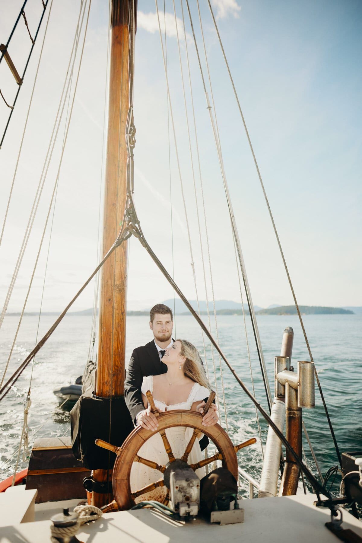 Newlyweds at the ship's wheel of a sailboat, dog beside them