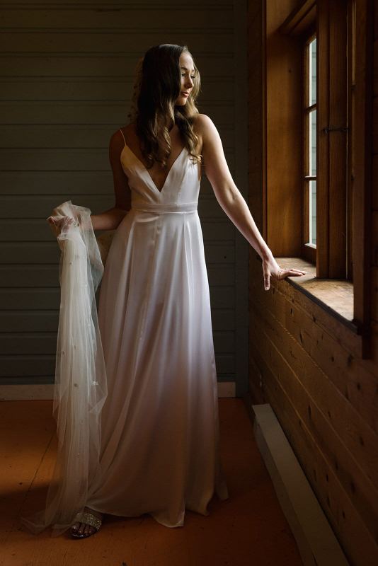 Bride holding her veil beside a warm cabin window