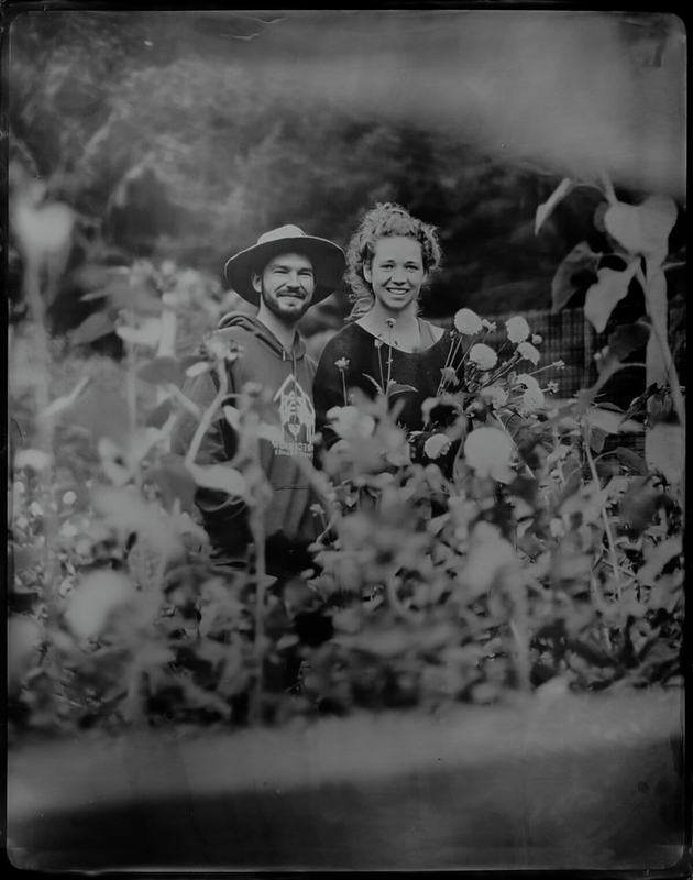 Smiling pair peeking through tall garden blooms, wet-plate style