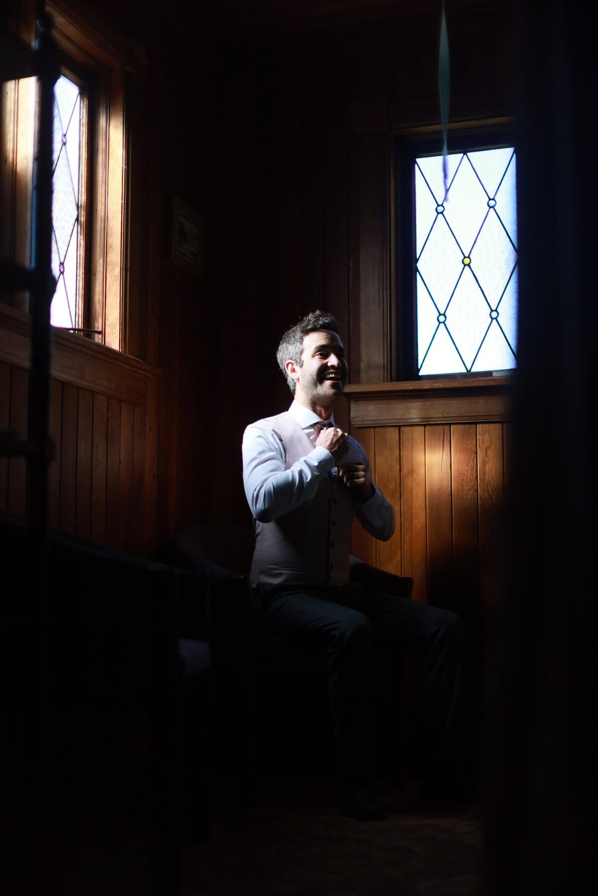 Groom buttoning his vest in a wood-panelled room