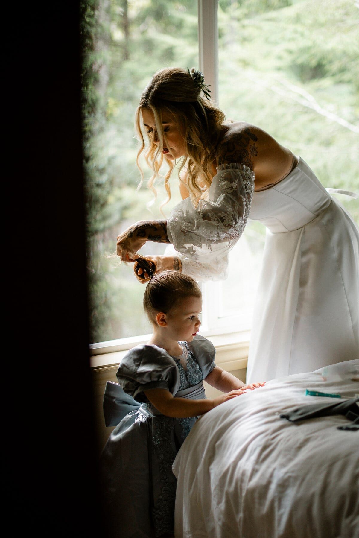 Bride brushing a little girl's hair beside a bright window