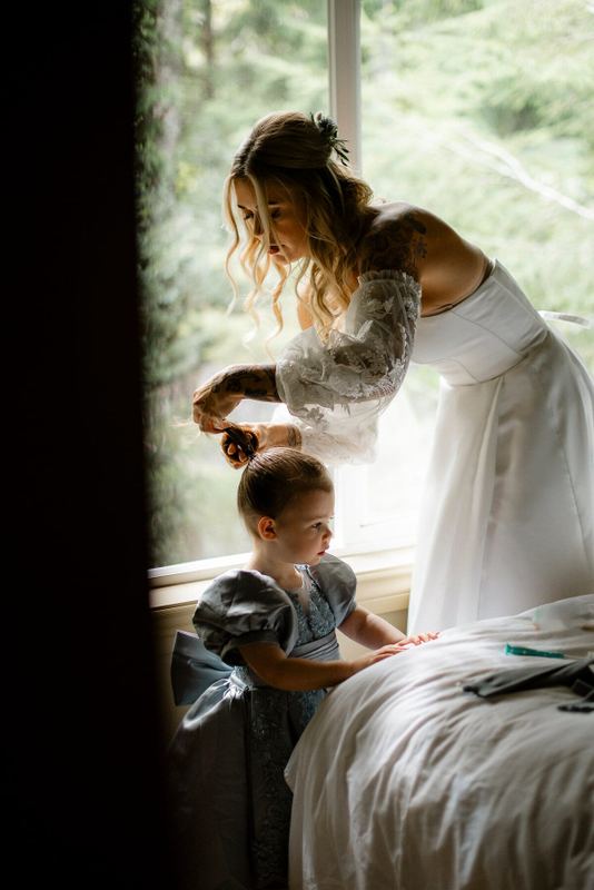 Bride brushing a little girl's hair beside a bright window