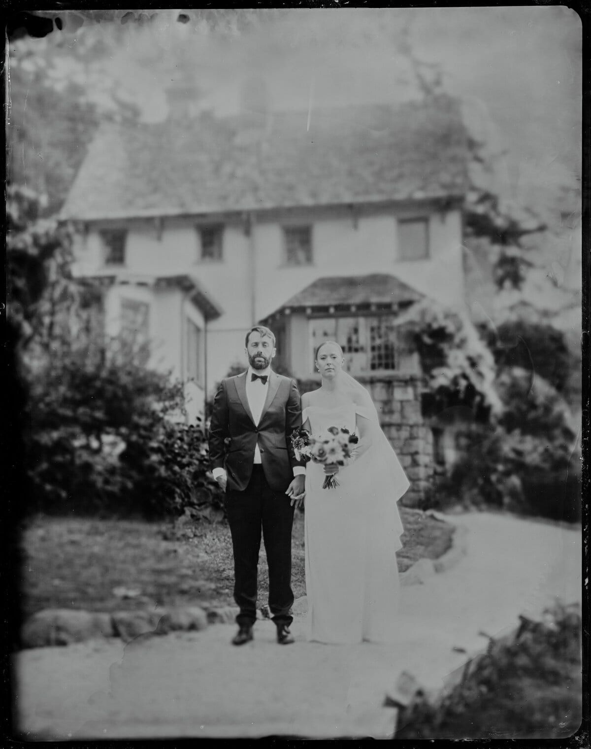 Tintype of newlyweds standing before a storybook cottage